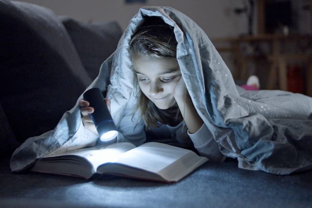 Garota lendo livro com lanterna