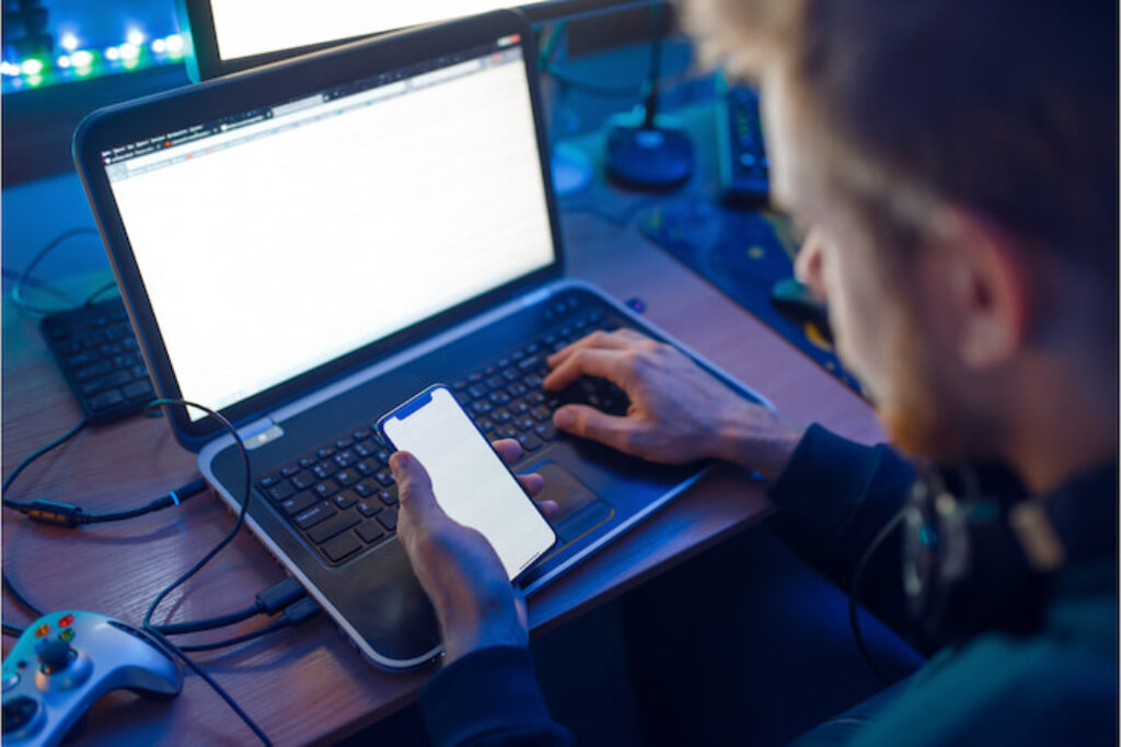 Pessoa com o celular na mão enquanto digita em um notebook